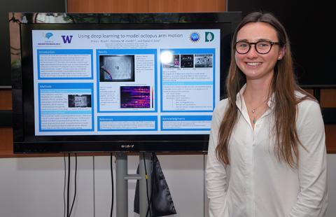 A young woman stands smiling in front of a research poster