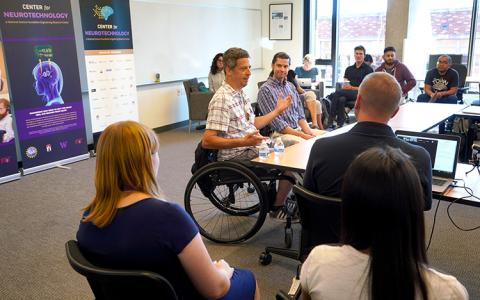 A man in a wheelchair talking to a group of people at a table