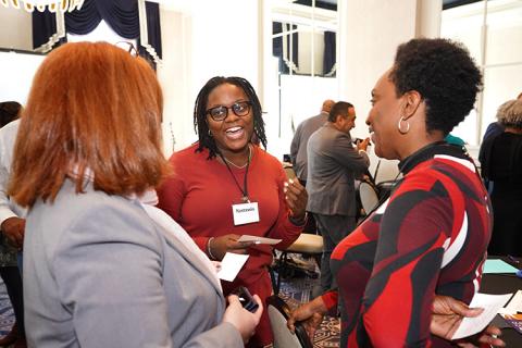 Three people stand in a circle and smile at each other as they talk.