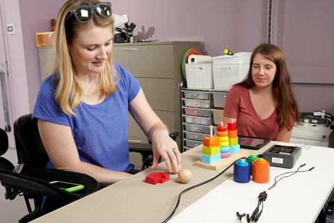 Jessica Owen performs a series of exercises involving putting differently-shaped blocks on wooden pegs while electrical stimulation is being applied to her spine. Megan Knoernschild, undergraduate researcher in the Moritz Lab, oversees. This form of physical therapy is designed to develop and restore fine motor skills in Owen’s hands.