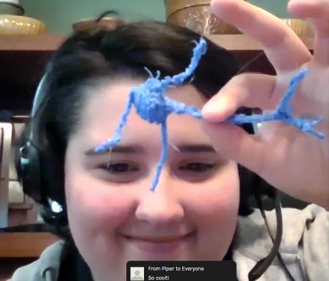 A young girl holds up a neuron model she made out of pipe cleaners