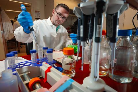 Research Experience for Veterans (REV) participant, Joshua Dreessen, working in the CNT-affiliated Perlmutter lab. Dreesen is currently an undergraduate at the University of Washington (UW) studying neuroscience. Man in lab coat working with tubes and bottles in a lab