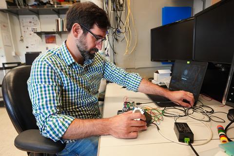 A man, sitting at a desk, working on electronic equipment