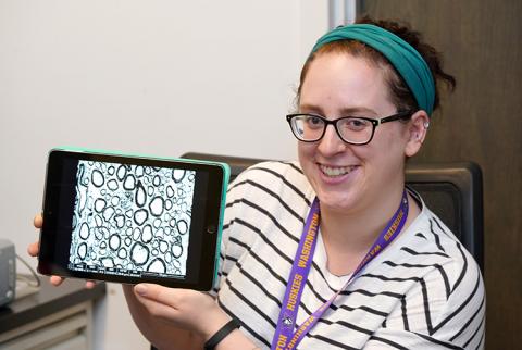 A young woman holds up an iPad that is showing a photo.