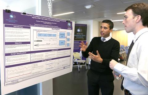 A young man explains the content of his research poster to another young man