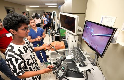 Students in the YSP-REACH program visit the WWAMI Institute for Simulation in Healthcare, a surgical training facility used for health care education. Here, a student experiments with a device designed to train medical personnel in remote surgery. A young man operates a device with levers attached to a monitor.