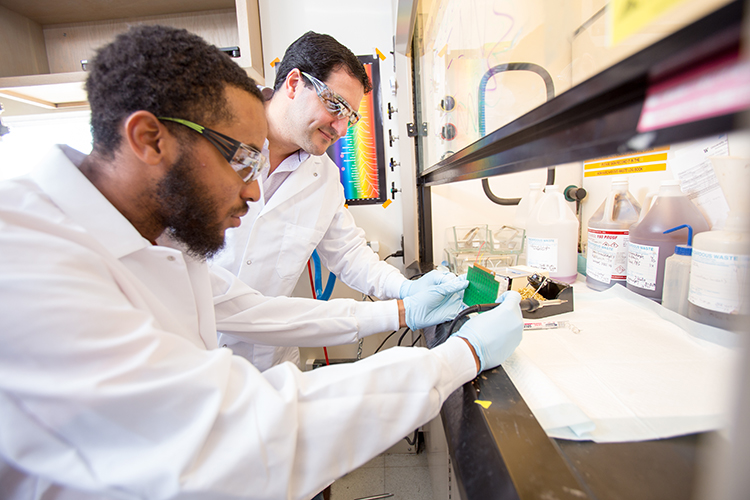 Two researchers in lab coats work on a microcontroller board