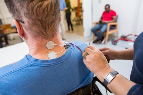 Man sitting in chair with stimulating electrodes on his neck.